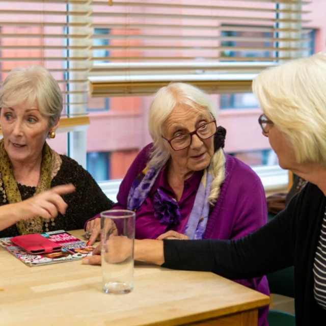 Image shows three older women at a table in discussion